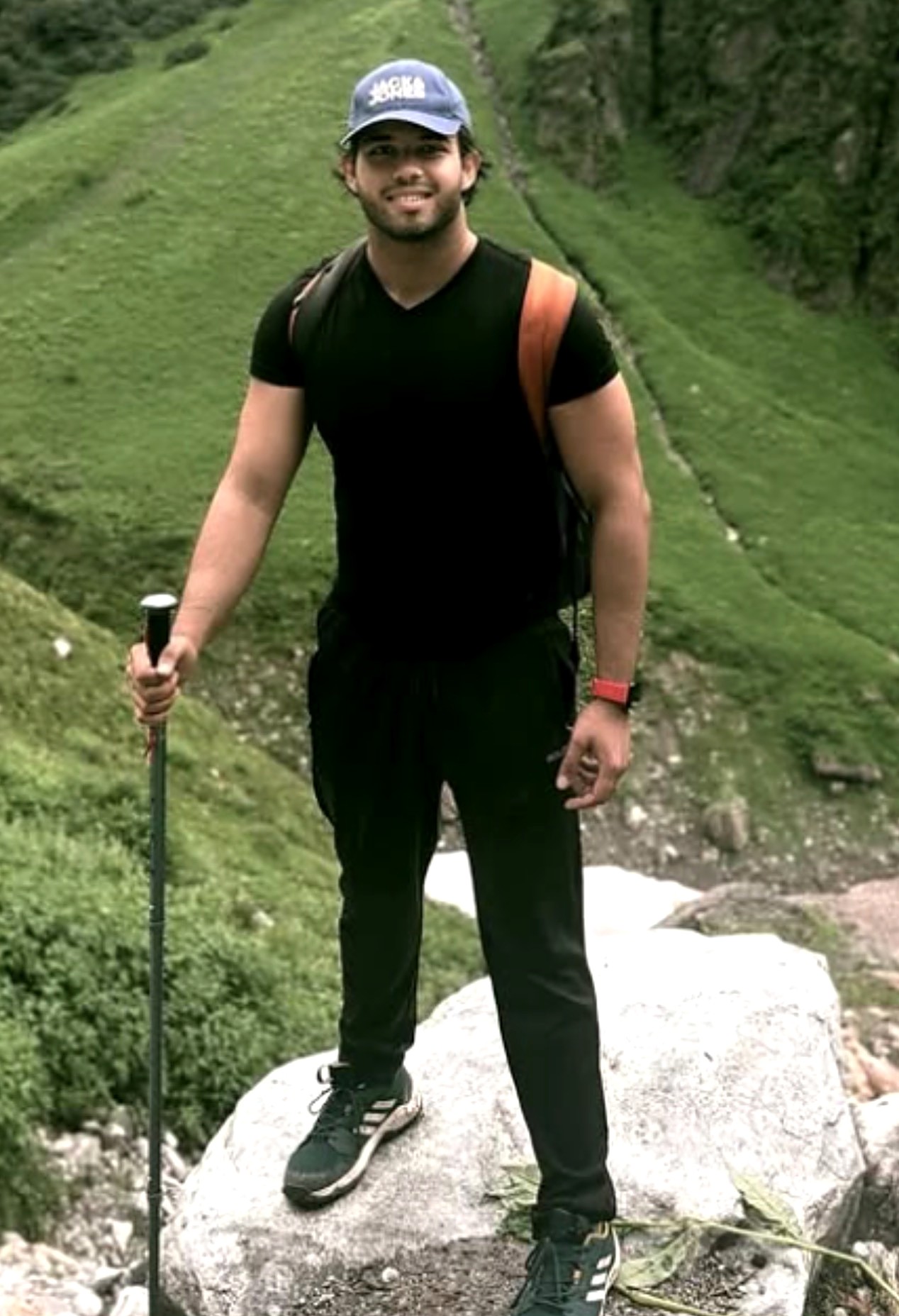 Swarnava Mallik smiling on a mountain trek, standing on a rock with a trekking pole